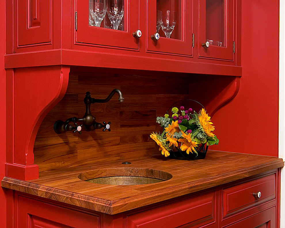 Klassische Wohnküche in U-Form mit profilierten Schrankfronten, roten Schränken, Arbeitsplatte aus Holz, Küchenrückwand in Braun, dunklem Holzboden und Kücheninsel in Sonstige