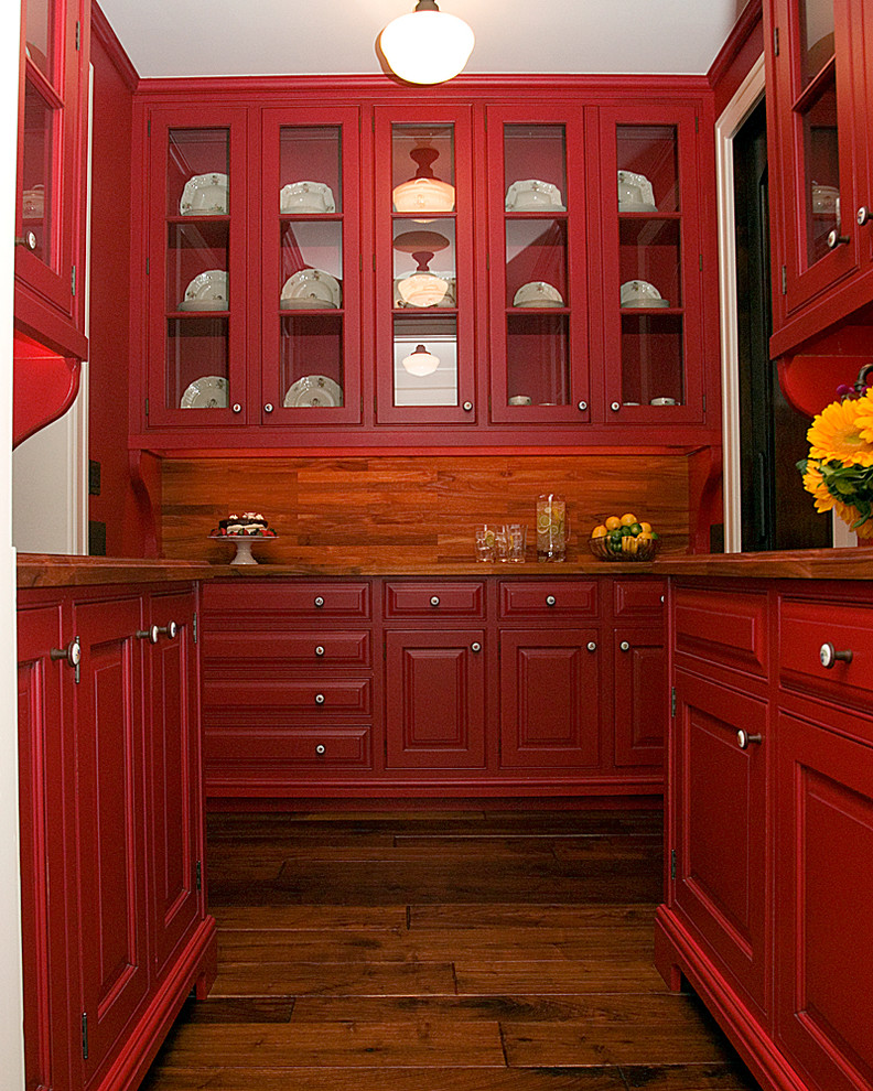 Klassische Wohnküche in U-Form mit profilierten Schrankfronten, roten Schränken, Arbeitsplatte aus Holz, Küchenrückwand in Braun, dunklem Holzboden und Kücheninsel in Sonstige