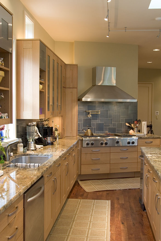 Cette image montre une cuisine design en bois clair avec un plan de travail en granite, un évier 2 bacs, une crédence bleue et un électroménager en acier inoxydable.