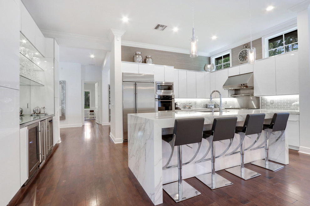 Huge minimalist galley eat-in kitchen photo in Miami with a farmhouse sink, flat-panel cabinets, white cabinets, white backsplash, stainless steel appliances, an island and white countertops