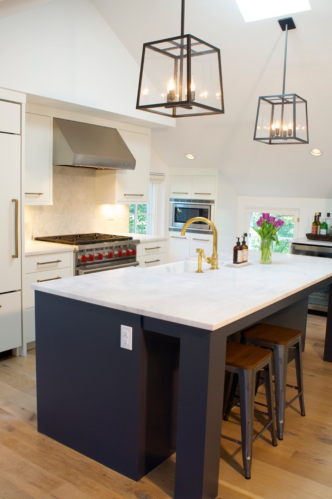 Photo of a modern galley kitchen in Denver with a belfast sink, flat-panel cabinets, integrated appliances, light hardwood flooring and an island.