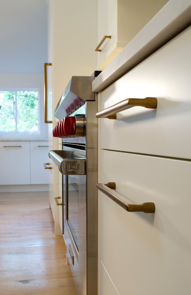Zweizeilige Moderne Küche mit Landhausspüle, flächenbündigen Schrankfronten, Elektrogeräten mit Frontblende, hellem Holzboden und Kücheninsel in Denver