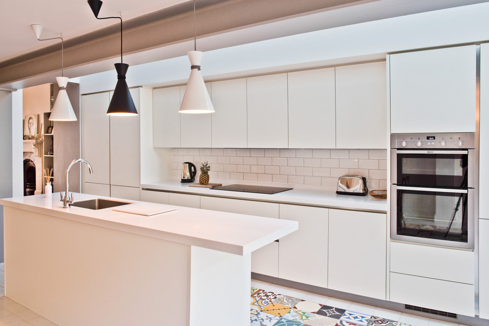 Inspiration for a contemporary galley kitchen in London with a submerged sink, flat-panel cabinets, white cabinets, white splashback, metro tiled splashback, stainless steel appliances and an island.