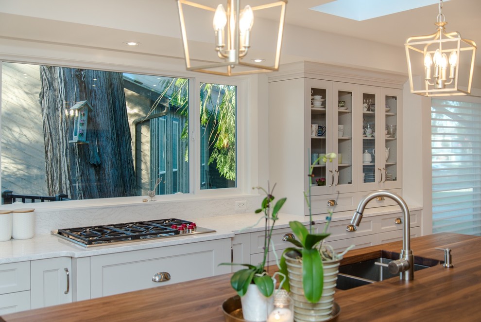 Inspiration for a medium sized traditional kitchen/diner in Vancouver with a double-bowl sink, shaker cabinets, white cabinets, engineered stone countertops, white splashback, metro tiled splashback, stainless steel appliances, medium hardwood flooring, an island, beige floors and white worktops.
