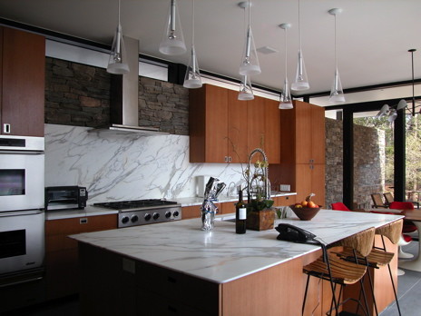 Example of a minimalist l-shaped slate floor and gray floor eat-in kitchen design in New York with flat-panel cabinets, medium tone wood cabinets, white backsplash, marble backsplash, stainless steel appliances and an island