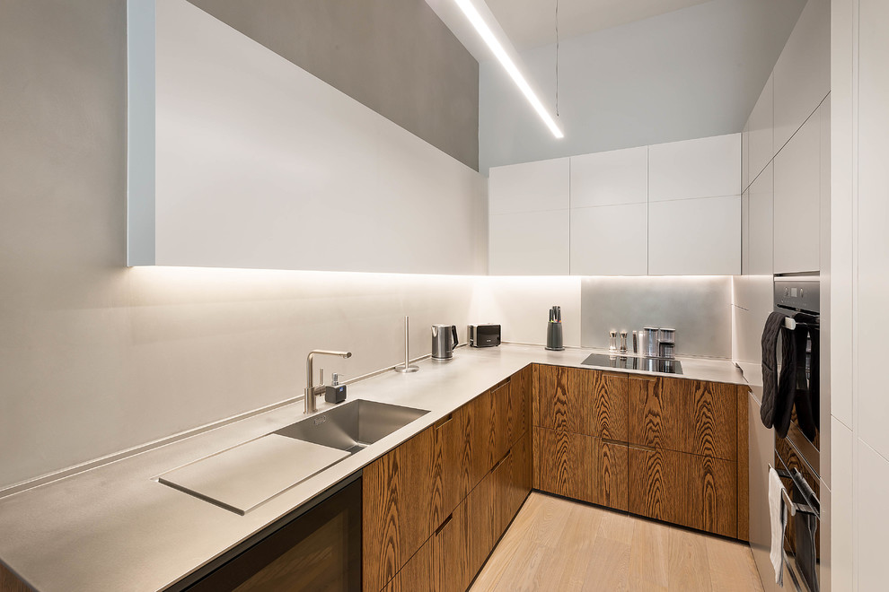 Foto på ett funkis l-kök, med en integrerad diskho, släta luckor, vita skåp, bänkskiva i rostfritt stål, ljust trägolv och beiget golv