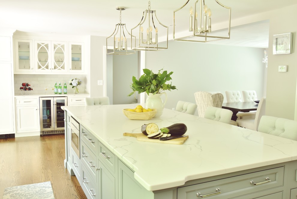 Klassisk inredning av ett vit vitt kök, med en rustik diskho, luckor med profilerade fronter, bänkskiva i kvarts, vitt stänkskydd, stänkskydd i marmor, rostfria vitvaror, mörkt trägolv och en köksö