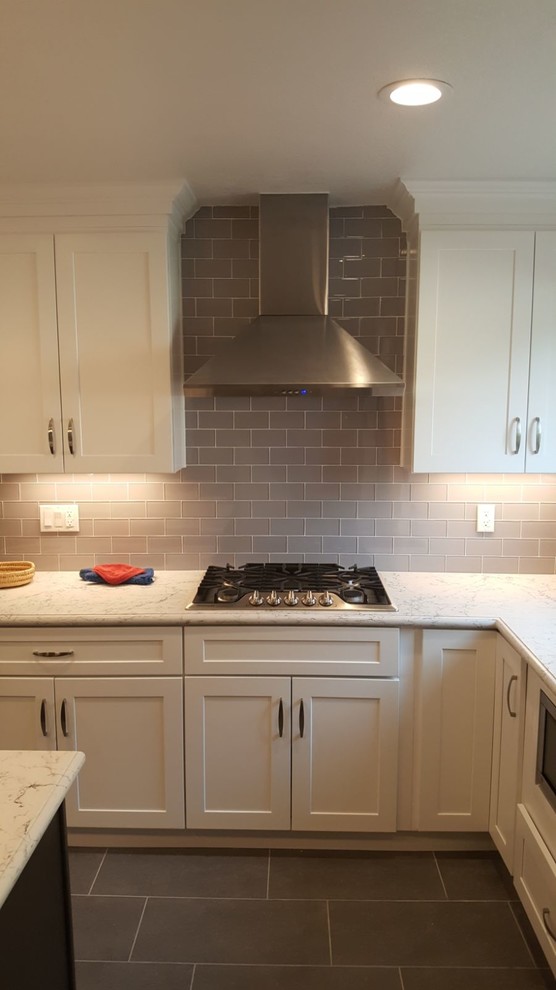 This is an example of a large classic l-shaped kitchen/diner in Los Angeles with a built-in sink, shaker cabinets, light wood cabinets, quartz worktops, glass tiled splashback, stainless steel appliances, ceramic flooring, an island, grey splashback, black floors and white worktops.