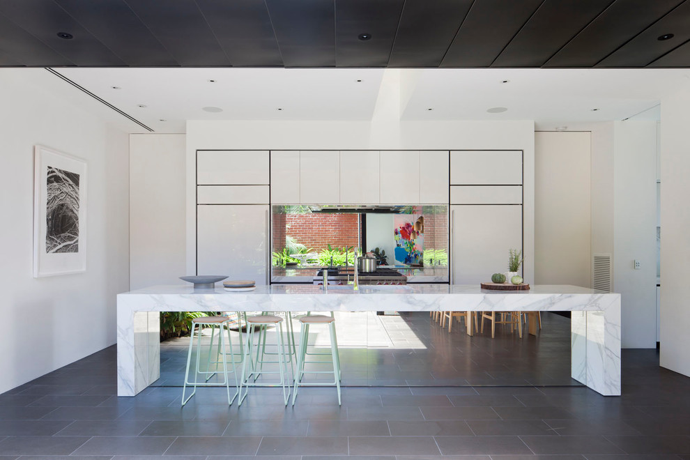 Zweizeilige Moderne Küche mit flächenbündigen Schrankfronten, weißen Schränken, Küchenrückwand in Metallic, Rückwand aus Spiegelfliesen, Elektrogeräten mit Frontblende, Kücheninsel, grauem Boden und weißer Arbeitsplatte in Melbourne
