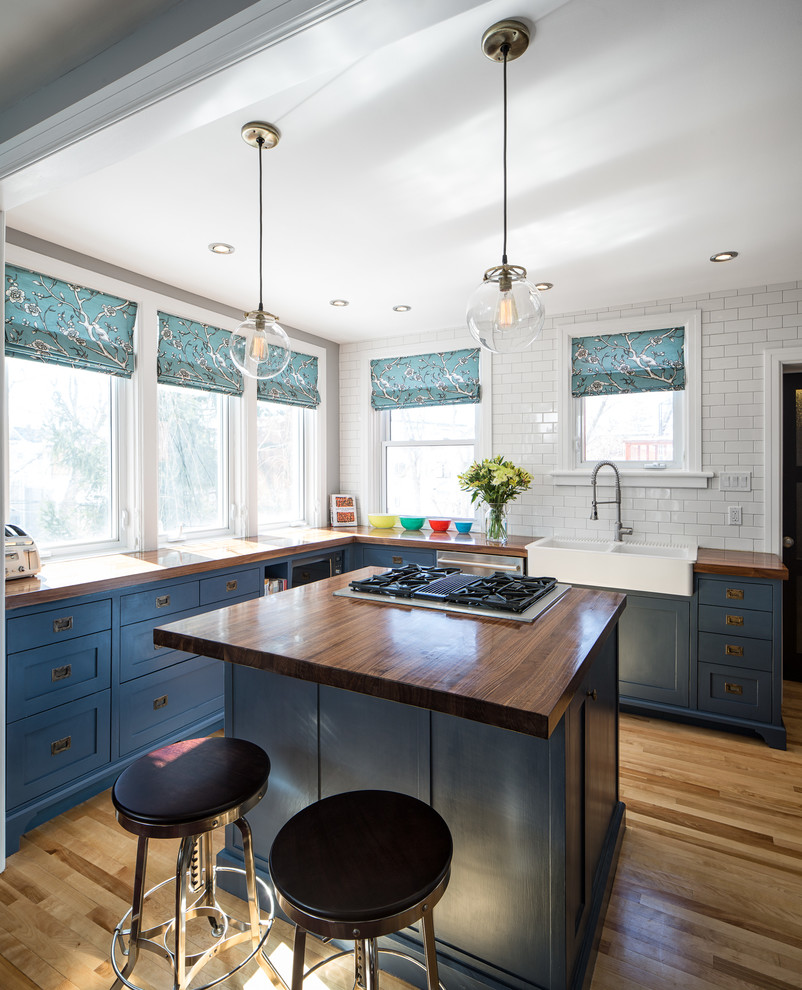 Inspiration for a traditional u-shaped kitchen/diner in Ottawa with a belfast sink, recessed-panel cabinets, wood worktops, white splashback, ceramic splashback, stainless steel appliances, medium hardwood flooring and an island.
