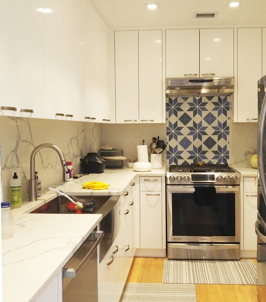 This is an example of a small midcentury l-shaped enclosed kitchen in New York with a submerged sink, flat-panel cabinets, white cabinets, engineered stone countertops, blue splashback, cement tile splashback, stainless steel appliances, light hardwood flooring, no island, brown floors and white worktops.
