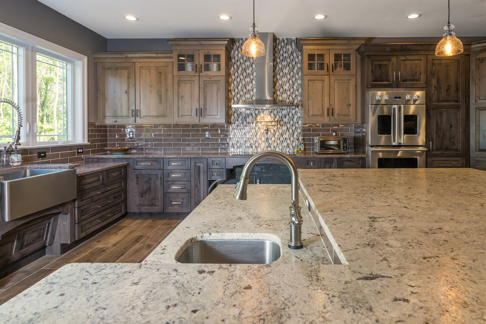Large mountain style l-shaped porcelain tile and brown floor open concept kitchen photo in Philadelphia with a farmhouse sink, raised-panel cabinets, distressed cabinets, quartz countertops, gray backsplash, cement tile backsplash, stainless steel appliances and an island