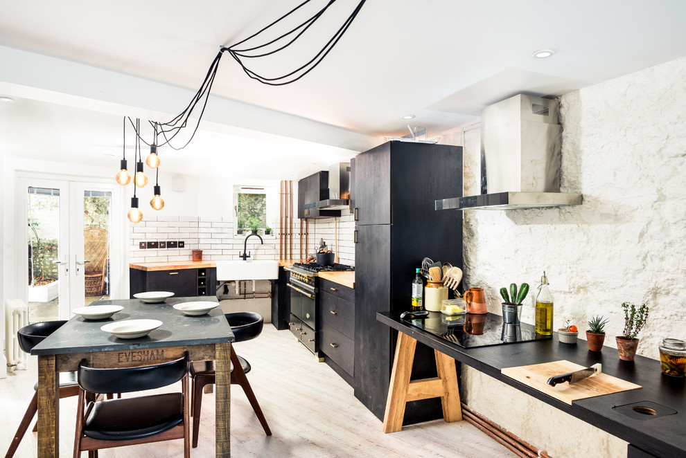 Inspiration for a scandi l-shaped kitchen/diner in Sussex with a belfast sink, flat-panel cabinets, black cabinets, wood worktops, white splashback, black appliances, light hardwood flooring and beige floors.