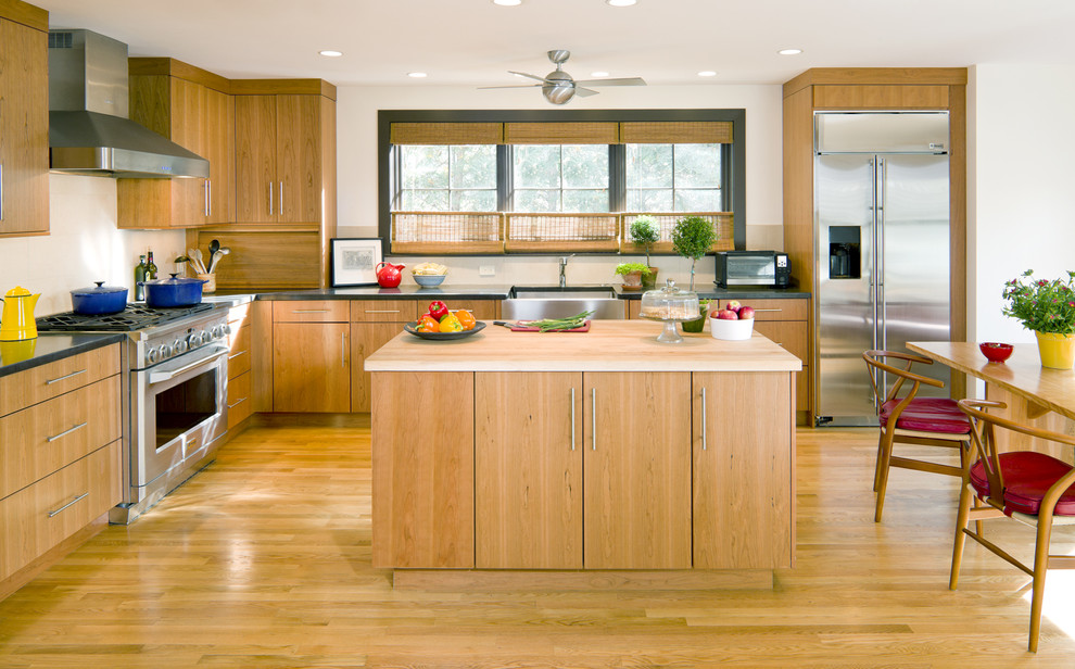 Example of a trendy l-shaped kitchen design in Boston with stainless steel appliances, a farmhouse sink, flat-panel cabinets and medium tone wood cabinets