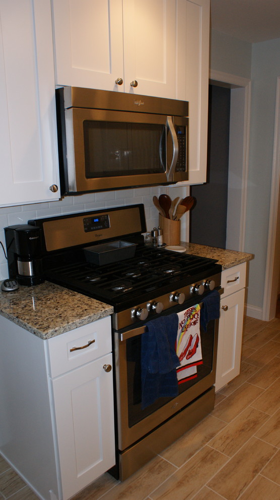 Klassisk inredning av ett kök, med en undermonterad diskho, skåp i shakerstil, vita skåp, granitbänkskiva, vitt stänkskydd, stänkskydd i tunnelbanekakel och rostfria vitvaror