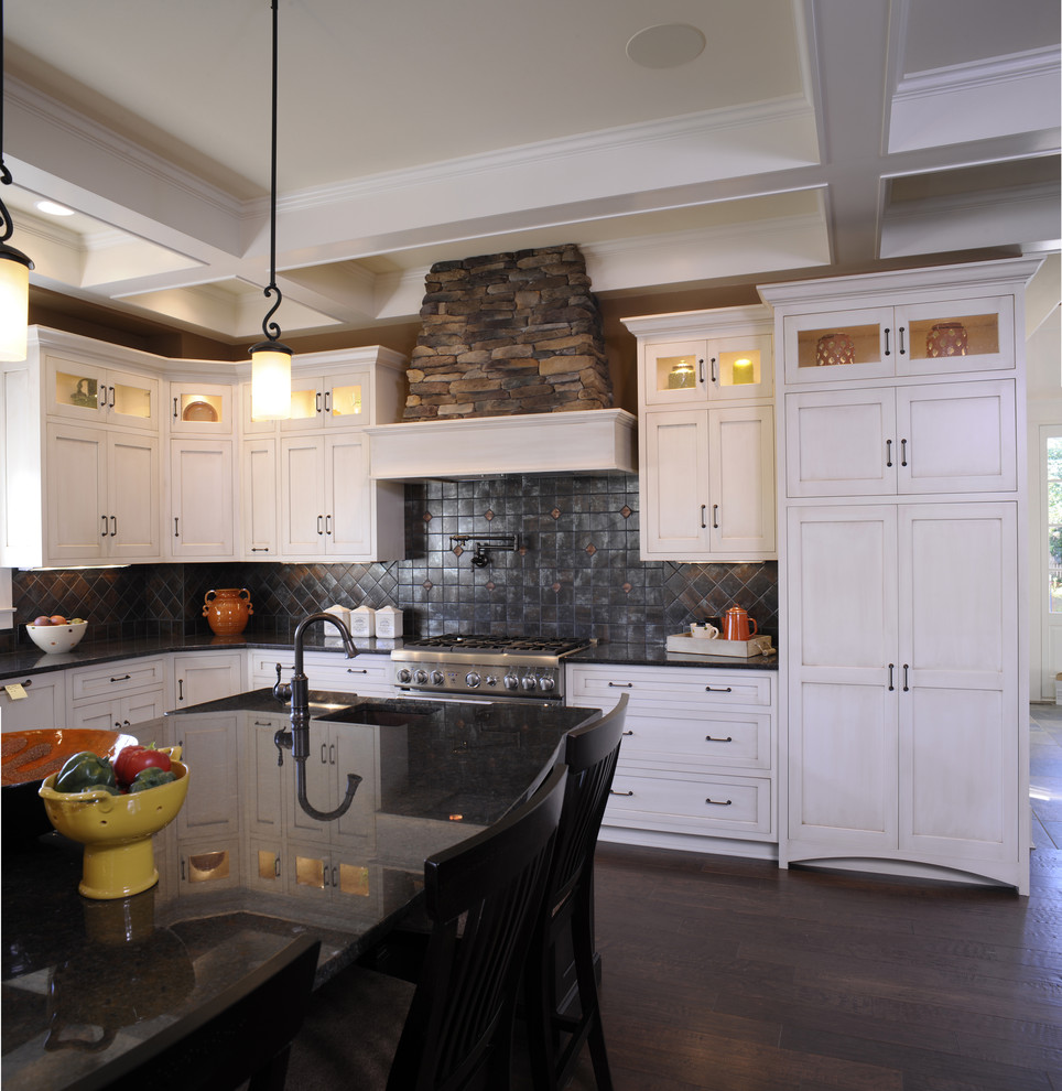Photo of a rustic l-shaped kitchen/diner in Columbus with white cabinets, black splashback, shaker cabinets, stainless steel appliances, dark hardwood flooring, an island, black worktops, a coffered ceiling and a belfast sink.