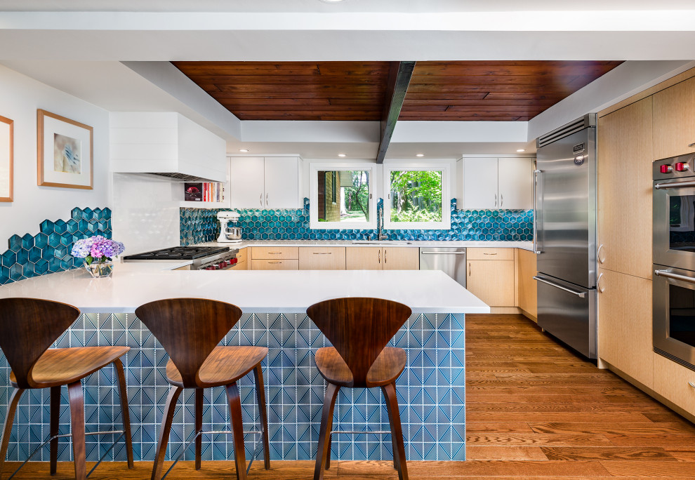 Immagine di una cucina minimalista con ante lisce, ante in legno chiaro, paraspruzzi blu, paraspruzzi con piastrelle di vetro, elettrodomestici in acciaio inossidabile, parquet scuro, top bianco e soffitto in legno