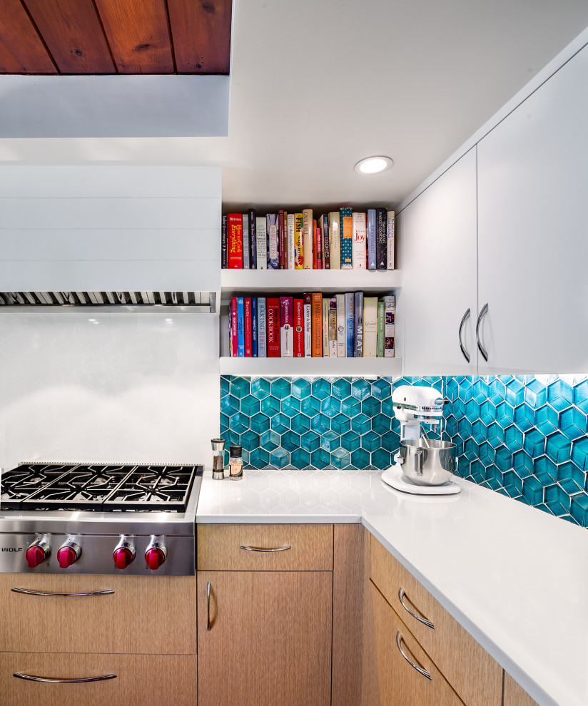 Immagine di una cucina ad U moderna con ante lisce, ante in legno chiaro, paraspruzzi blu, paraspruzzi con piastrelle di vetro, elettrodomestici in acciaio inossidabile, parquet scuro, top bianco e soffitto in legno