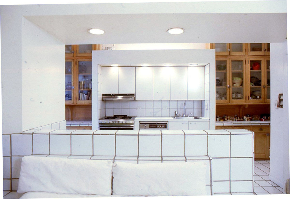 ニューヨークにあるラグジュアリーな巨大なおしゃれなキッチン (ドロップインシンク、フラットパネル扉のキャビネット、中間色木目調キャビネット、タイルカウンター、白いキッチンパネル、セラミックタイルのキッチンパネル、パネルと同色の調理設備、セラミックタイルの床) の写真