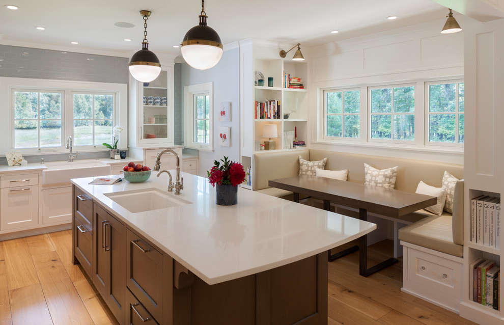 This is an example of a country kitchen/diner in Grand Rapids with light hardwood flooring, an island, white worktops, a belfast sink, shaker cabinets and white cabinets.