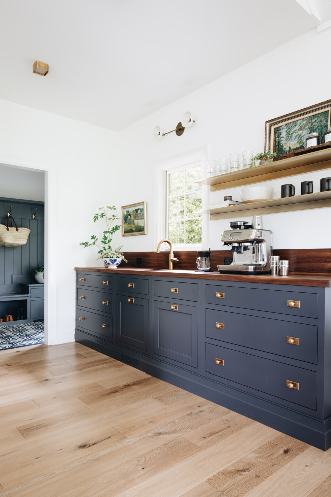 Exemple d'une cuisine chic en L avec un placard avec porte à panneau encastré, des portes de placard bleues, un plan de travail en bois, une crédence en marbre, parquet clair, îlot, un sol beige et un plan de travail marron.