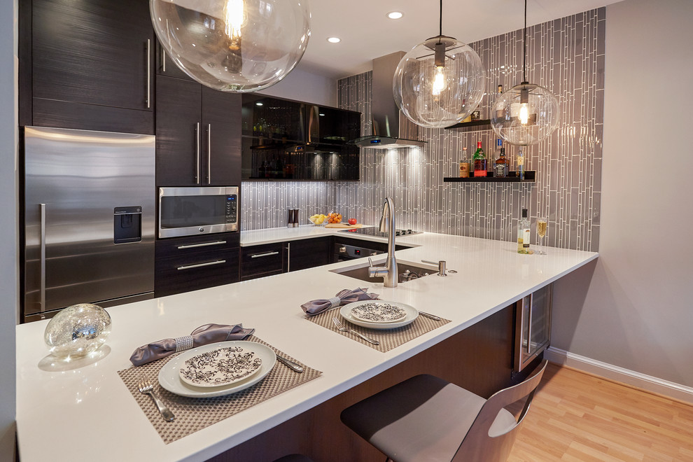 Foto di una cucina minimal con lavello sottopiano, ante lisce, ante nere, paraspruzzi grigio, elettrodomestici in acciaio inossidabile, parquet chiaro e penisola