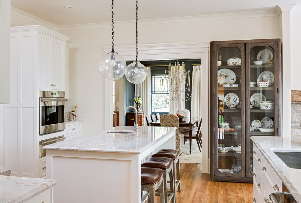Klassisk inredning av ett mellanstort kök, med en undermonterad diskho, skåp i shakerstil, vita skåp, granitbänkskiva, grått stänkskydd, stänkskydd i keramik, rostfria vitvaror, mellanmörkt trägolv och en köksö