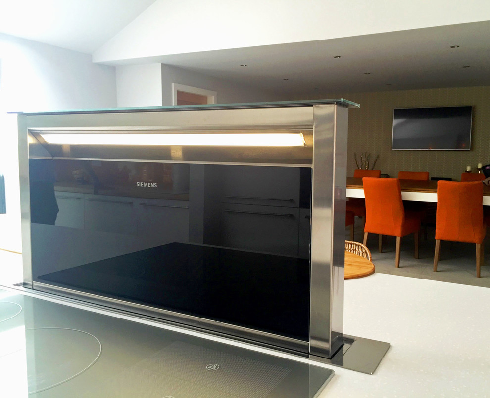 Imagen de cocina minimalista grande abierta con fregadero integrado, armarios con paneles lisos, salpicadero naranja, salpicadero de vidrio templado, electrodomésticos negros y una isla