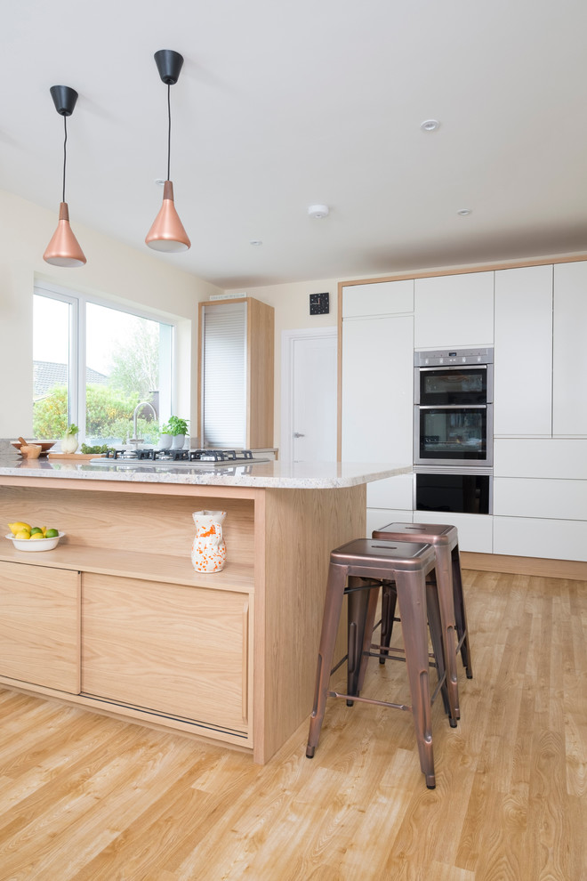 Modern inredning av ett mellanstort kök, med en undermonterad diskho, släta luckor, vita skåp, granitbänkskiva, rostfria vitvaror, mellanmörkt trägolv och en halv köksö