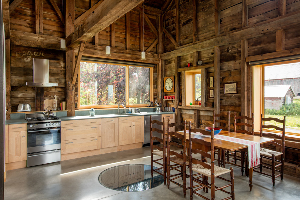 Imagen de cocina comedor lineal campestre sin isla con fregadero de un seno, armarios estilo shaker, puertas de armario de madera clara, electrodomésticos de acero inoxidable y suelo de cemento