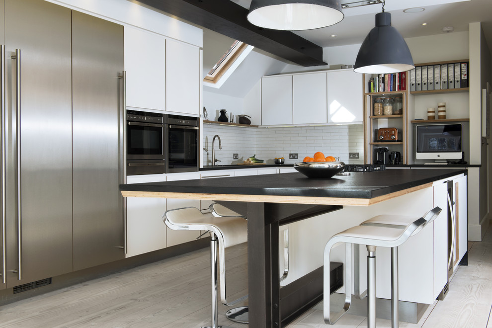 Diseño de cocinas en L nórdica con armarios con paneles lisos, suelo de madera clara, una isla, salpicadero blanco, electrodomésticos de acero inoxidable y con blanco y negro