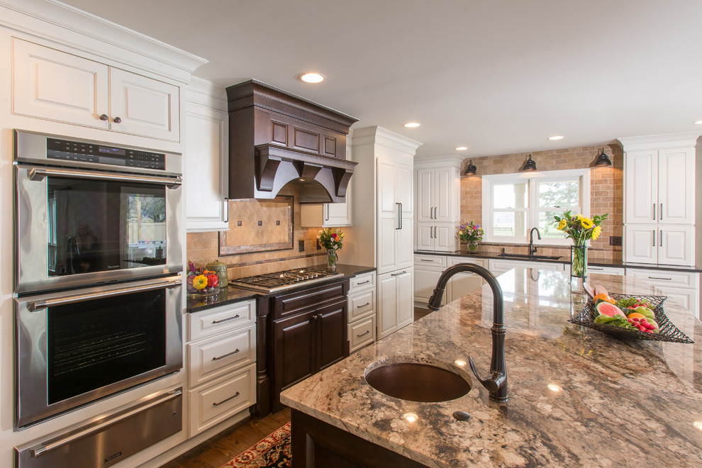 Inspiration for a large traditional l-shaped kitchen in Columbus with an undermount sink, raised-panel cabinets, white cabinets, granite benchtops, beige splashback, stone tile splashback, stainless steel appliances, medium hardwood floors and with island.