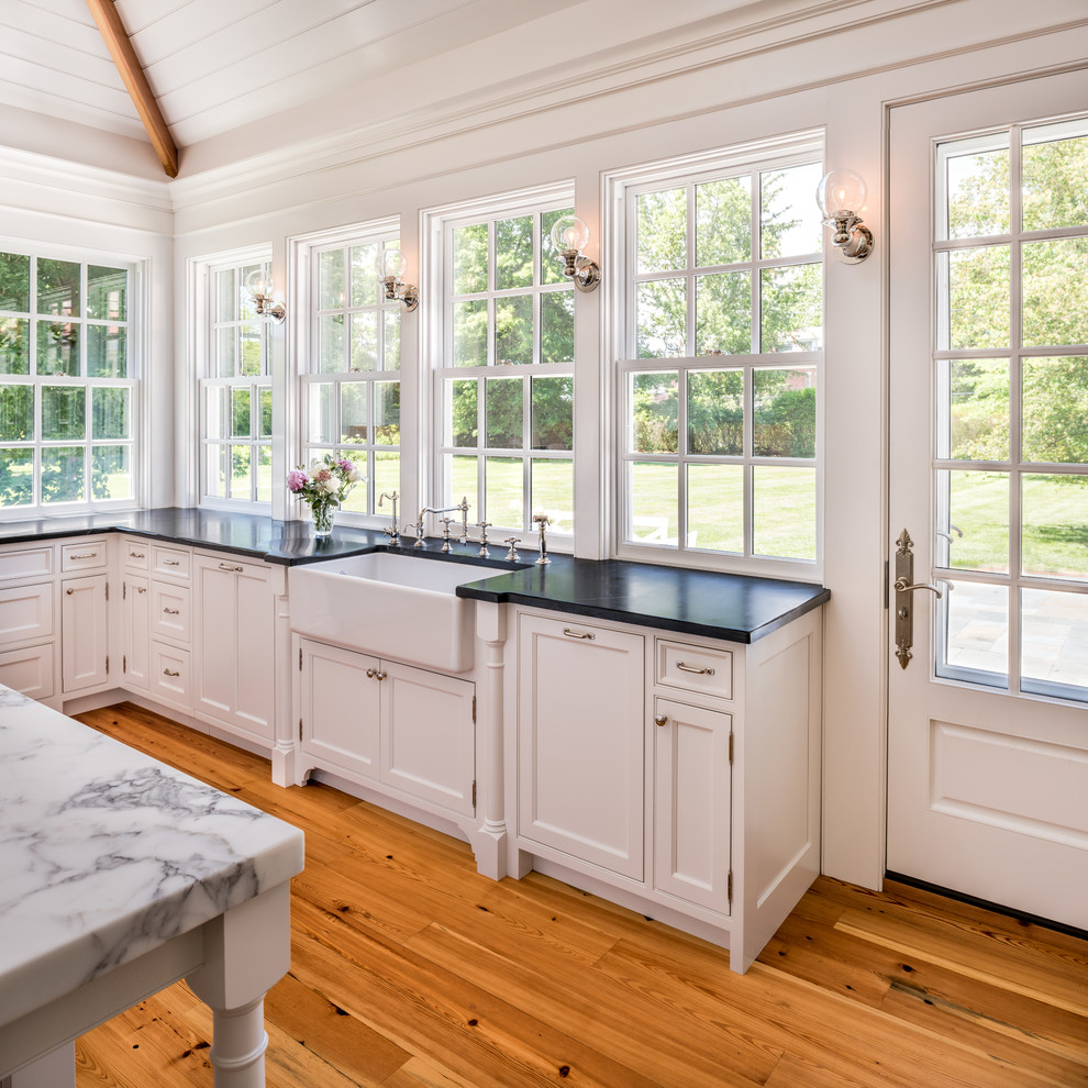 Example of a huge classic u-shaped light wood floor enclosed kitchen design in Philadelphia with a farmhouse sink, beaded inset cabinets, white cabinets, soapstone countertops, white backsplash, colored appliances and an island