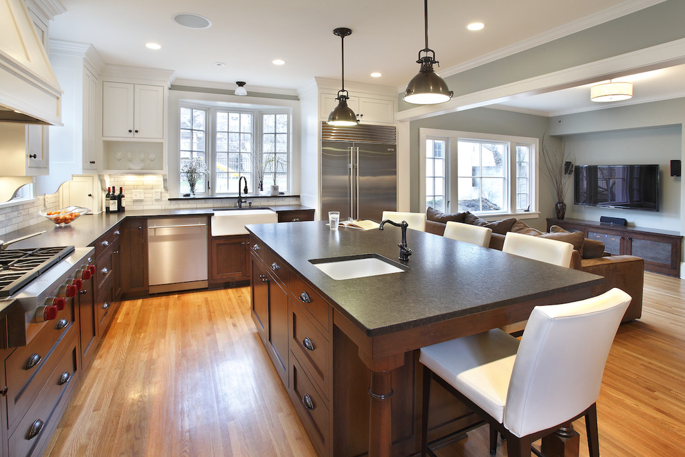 Photo of a large contemporary l-shaped kitchen/diner in Minneapolis with shaker cabinets, stainless steel appliances, an island, granite worktops, grey splashback, a belfast sink and light hardwood flooring.