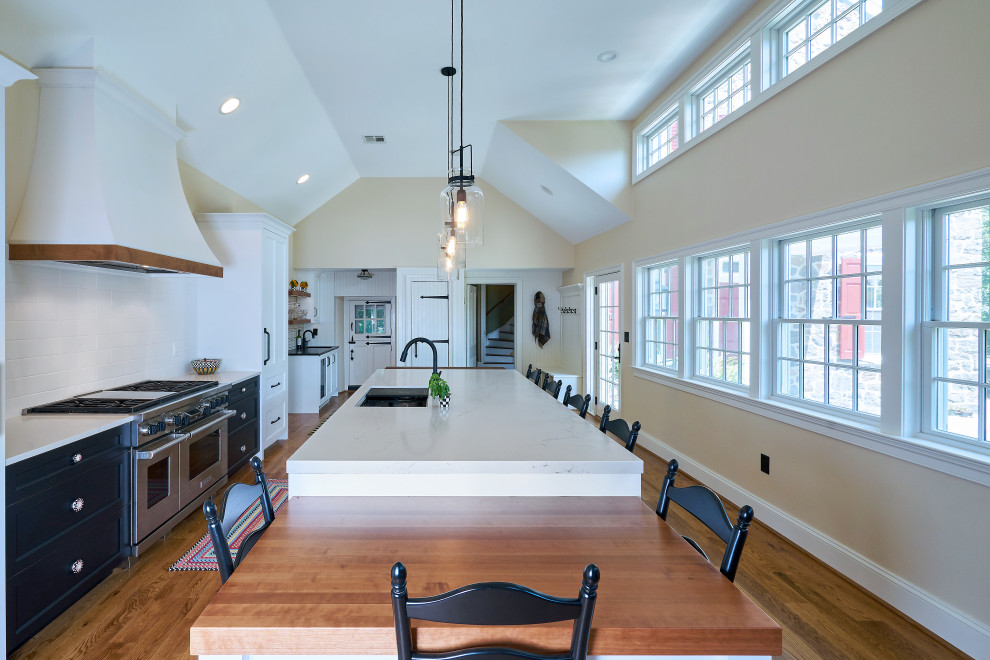 Inspiration for a large farmhouse medium tone wood floor and brown floor kitchen remodel in Philadelphia with an undermount sink, shaker cabinets, white cabinets, quartz countertops, white backsplash, porcelain backsplash, paneled appliances, an island and white countertops