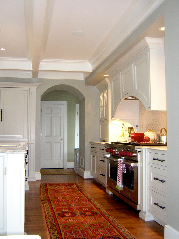 Example of a large classic u-shaped medium tone wood floor enclosed kitchen design in Other with an undermount sink, recessed-panel cabinets, white cabinets, granite countertops, white backsplash, stone slab backsplash, stainless steel appliances and an island