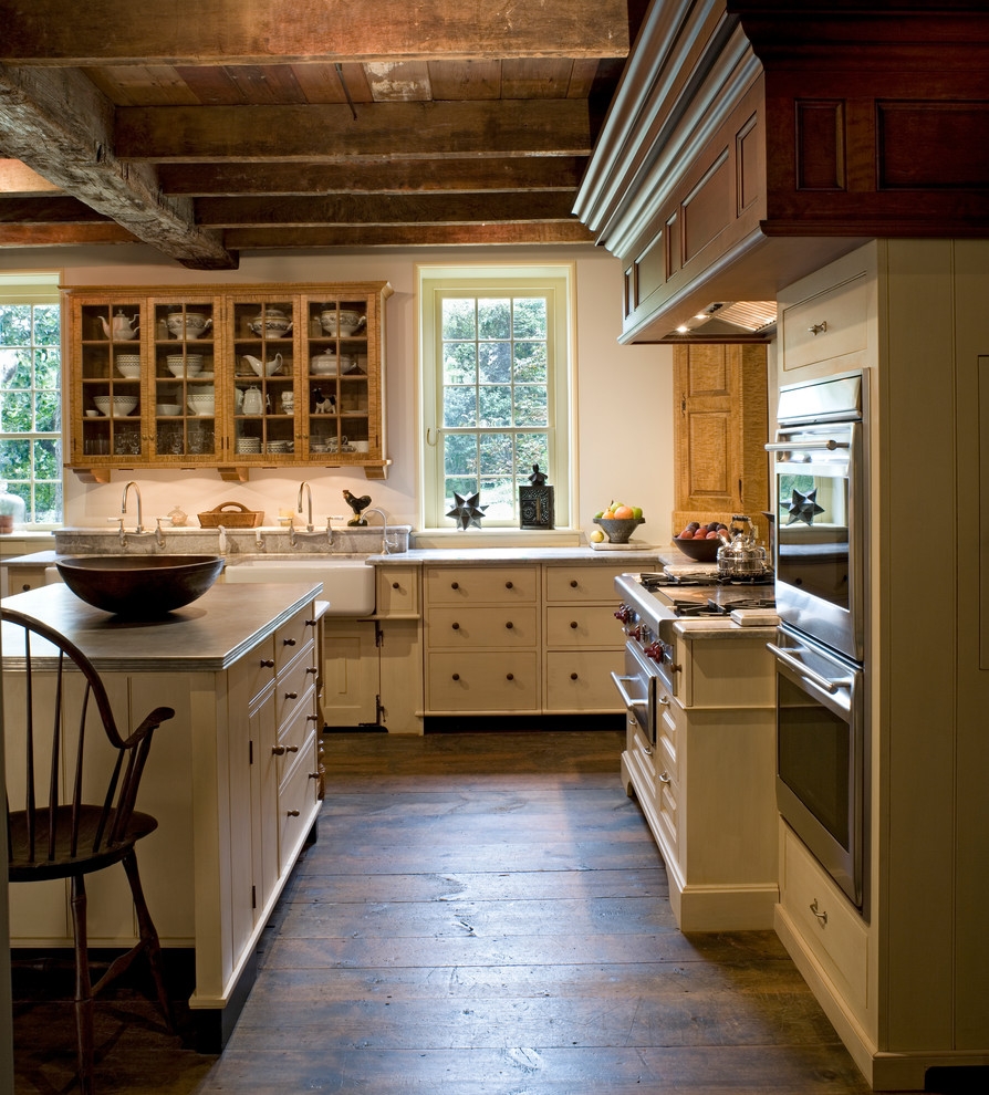 This is an example of a large farmhouse grey and cream l-shaped kitchen/diner in Philadelphia with a belfast sink, flat-panel cabinets, white cabinets, marble worktops, grey splashback, stone tiled splashback, stainless steel appliances, dark hardwood flooring, an island and brown floors.