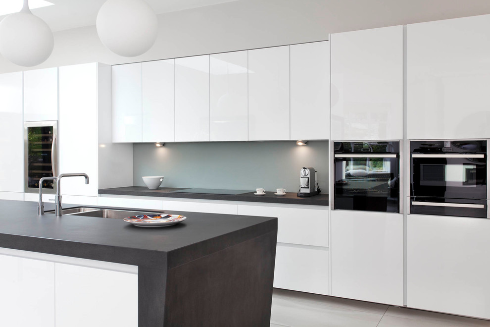 Inspiration for a large contemporary single-wall open plan kitchen in Belfast with a submerged sink, flat-panel cabinets, white cabinets, glass sheet splashback, integrated appliances, ceramic flooring, an island and white floors.