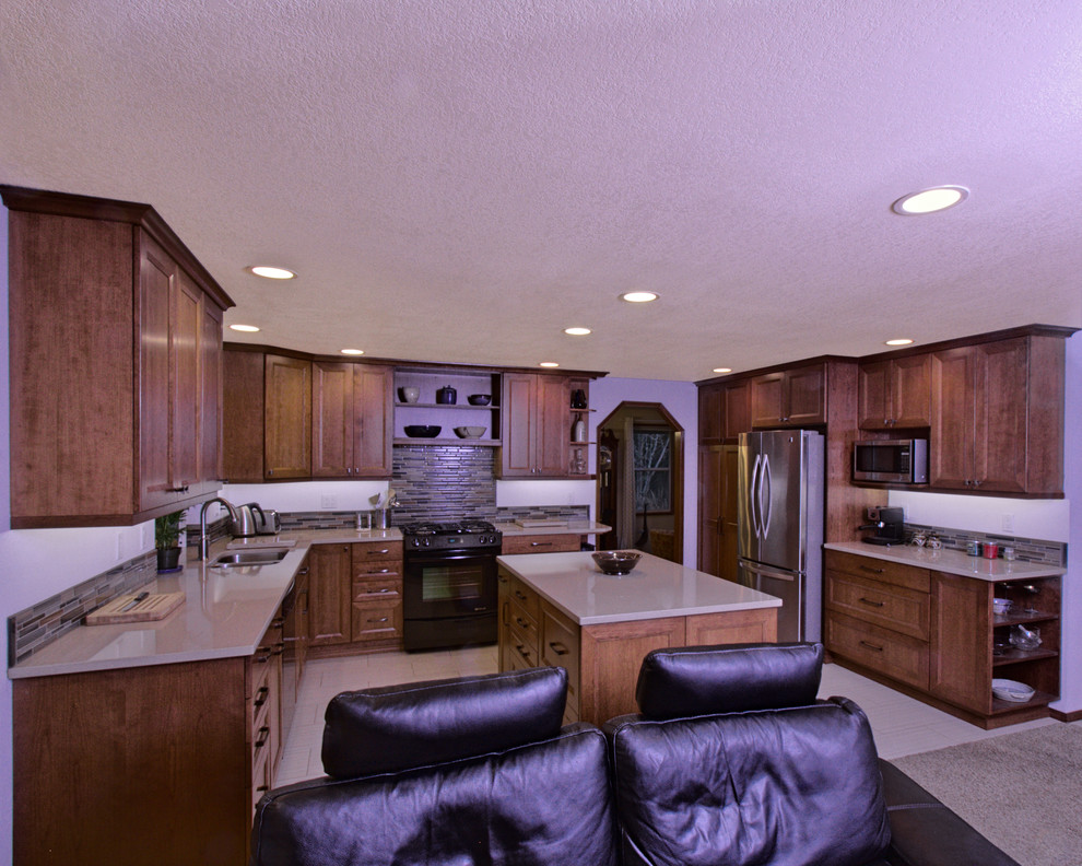 Exempel på ett klassiskt kök, med en dubbel diskho, luckor med infälld panel, skåp i mellenmörkt trä, bänkskiva i kvarts, grått stänkskydd, stänkskydd i glaskakel, svarta vitvaror och en köksö