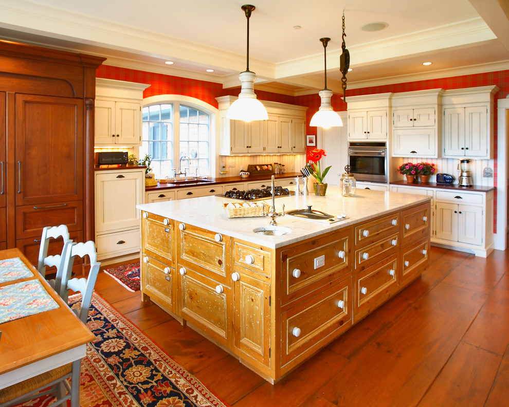 Amerikansk inredning av ett mellanstort kök, med en undermonterad diskho, luckor med infälld panel, vita skåp, vitt stänkskydd, mellanmörkt trägolv, en köksö, marmorbänkskiva, stänkskydd i trä, rostfria vitvaror och brunt golv