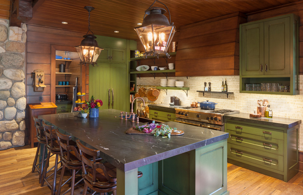 Expansive rustic kitchen in Grand Rapids with a belfast sink, shaker cabinets, green cabinets, beige splashback, stainless steel appliances, medium hardwood flooring, an island and black worktops.