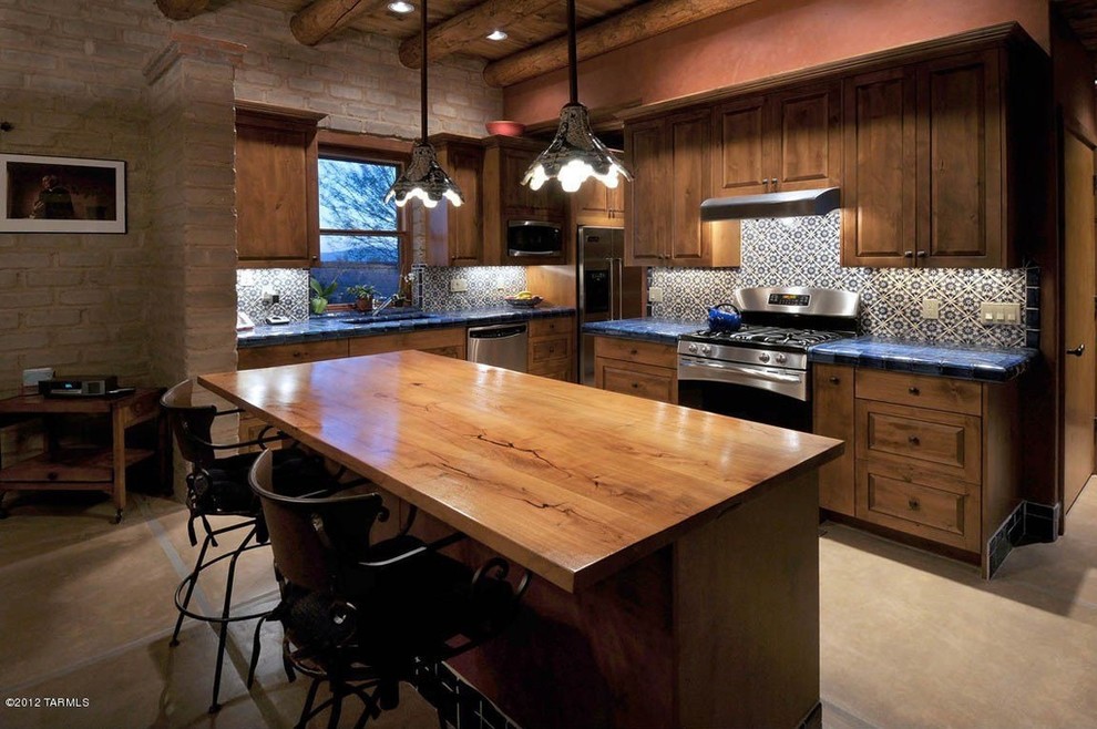 フェニックスにある高級な中くらいなサンタフェスタイルのおしゃれなキッチン (ダブルシンク、レイズドパネル扉のキャビネット、中間色木目調キャビネット、タイルカウンター、青いキッチンパネル、セラミックタイルのキッチンパネル、シルバーの調理設備、セラミックタイルの床) の写真