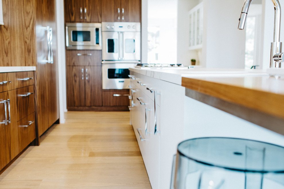 Modern inredning av ett mellanstort kök, med en undermonterad diskho, släta luckor, vita skåp, marmorbänkskiva, vitt stänkskydd, stänkskydd i sten, integrerade vitvaror, mellanmörkt trägolv och en köksö