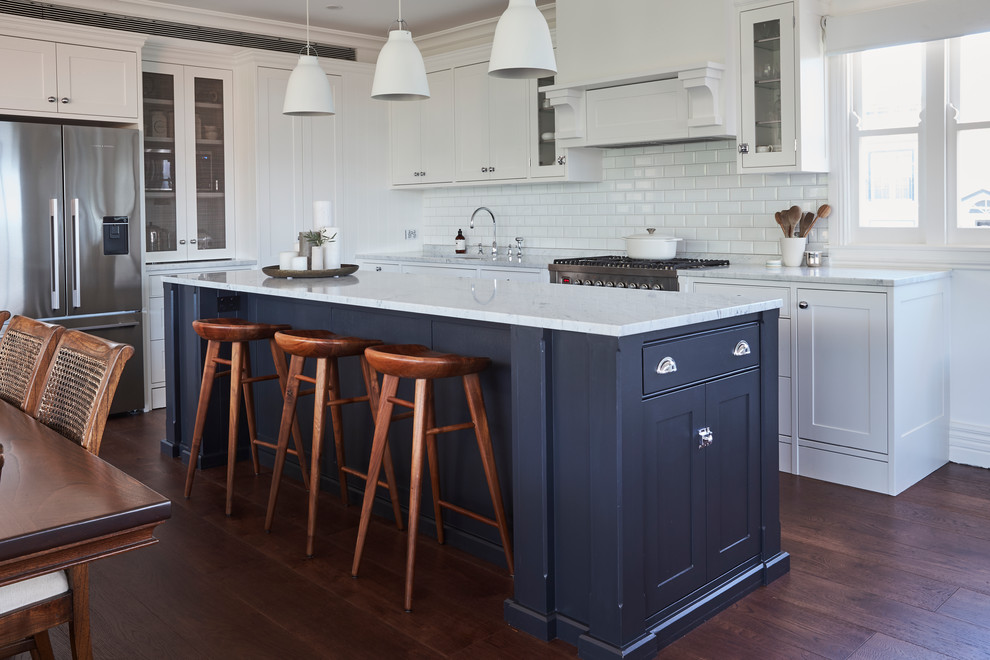 Traditional l-shaped kitchen/diner in Sydney with a submerged sink, shaker cabinets, blue cabinets, marble worktops, white splashback, metro tiled splashback, stainless steel appliances, medium hardwood flooring, an island, brown floors and white worktops.
