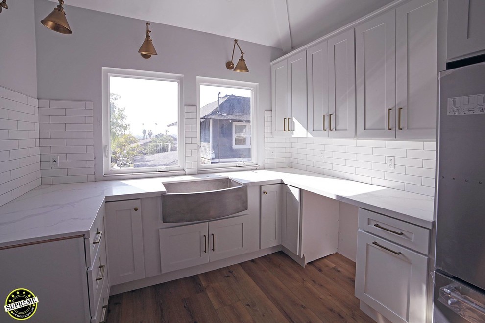 Inredning av ett modernt mellanstort vit vitt kök, med en rustik diskho, skåp i shakerstil, vita skåp, granitbänkskiva, vitt stänkskydd, stänkskydd i keramik, rostfria vitvaror, ljust trägolv och beiget golv