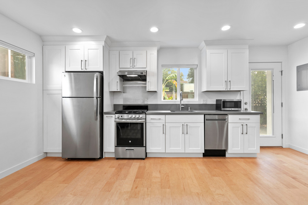 Exempel på ett mellanstort modernt grå linjärt grått kök med öppen planlösning, med en nedsänkt diskho, skåp i shakerstil, vita skåp, bänkskiva i betong, grått stänkskydd, stänkskydd i cementkakel, rostfria vitvaror, ljust trägolv och brunt golv