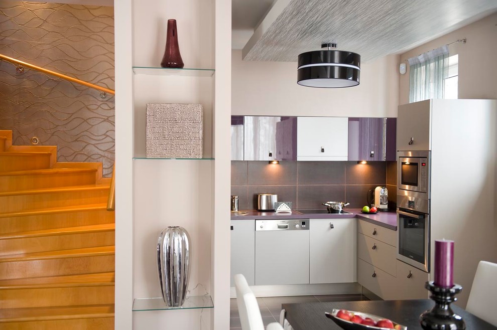 他の地域にあるコンテンポラリースタイルのおしゃれなダイニングキッチン (フラットパネル扉のキャビネット、パネルと同色の調理設備、グレーのキッチンパネル、石タイルのキッチンパネル、白いキャビネット、紫のキッチンカウンター) の写真