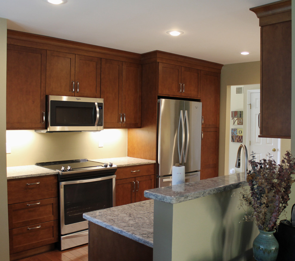 Inredning av ett klassiskt litet kök, med luckor med infälld panel, bruna skåp, rostfria vitvaror och ljust trägolv