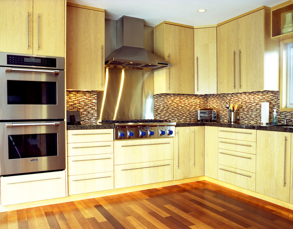 Cette photo montre une cuisine tendance en bois clair avec un plan de travail en granite, un placard à porte plane, une crédence multicolore, une crédence en carreau briquette et un électroménager en acier inoxydable.