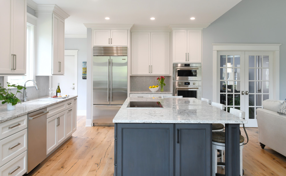 Mid-sized beach style l-shaped brown floor eat-in kitchen photo in Charleston with an undermount sink, flat-panel cabinets, white cabinets, solid surface countertops, white backsplash, porcelain backsplash, stainless steel appliances, an island and multicolored countertops